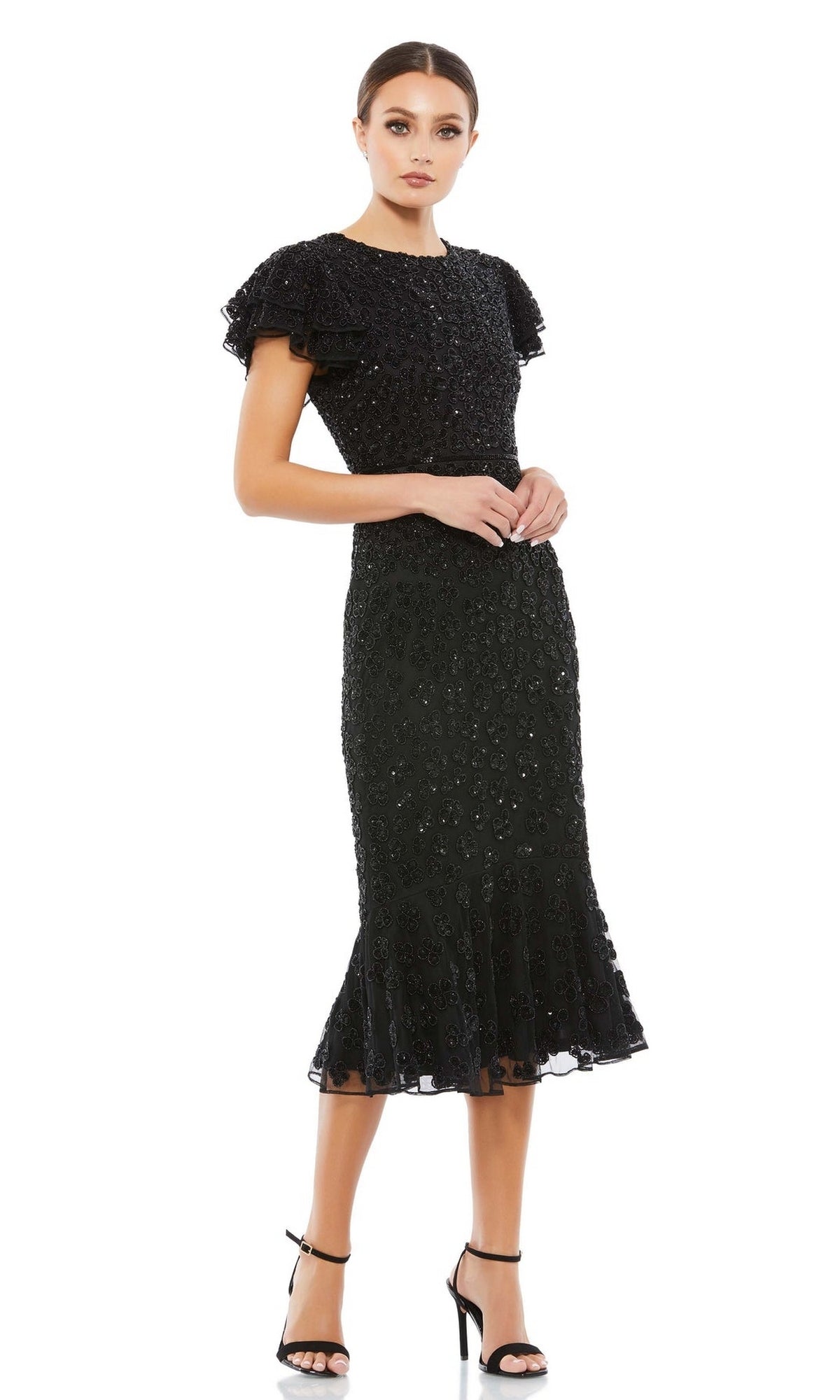 A woman wearing the Short Wedding Guest Dress 10771 by Mac Duggal, a black fitted midi dress with sequin embellishments and ruffled details, styled for a semi-formal look with black high-heeled sandals.